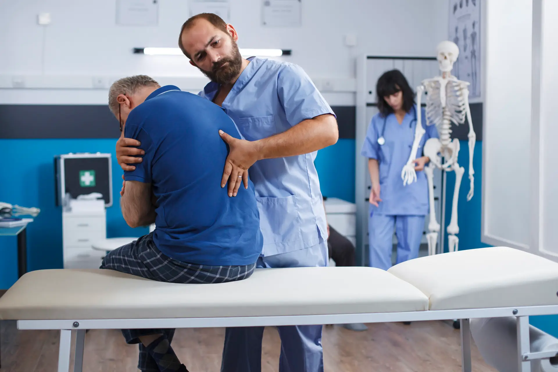 Osteopathic nurse gently extends spine of elderly patient with injury as part of physiotherapy. Chiropractor provides aid to gentleman experiencing back pains, aiding in physical recovery.